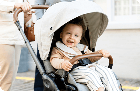 Smiling toddler in a Joie finiti Signature pushchair in a light gray.